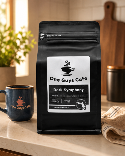 One Guys Cafe Dark Symphony dark roast coffee bag on a kitchen counter beside a branded mug and towel.