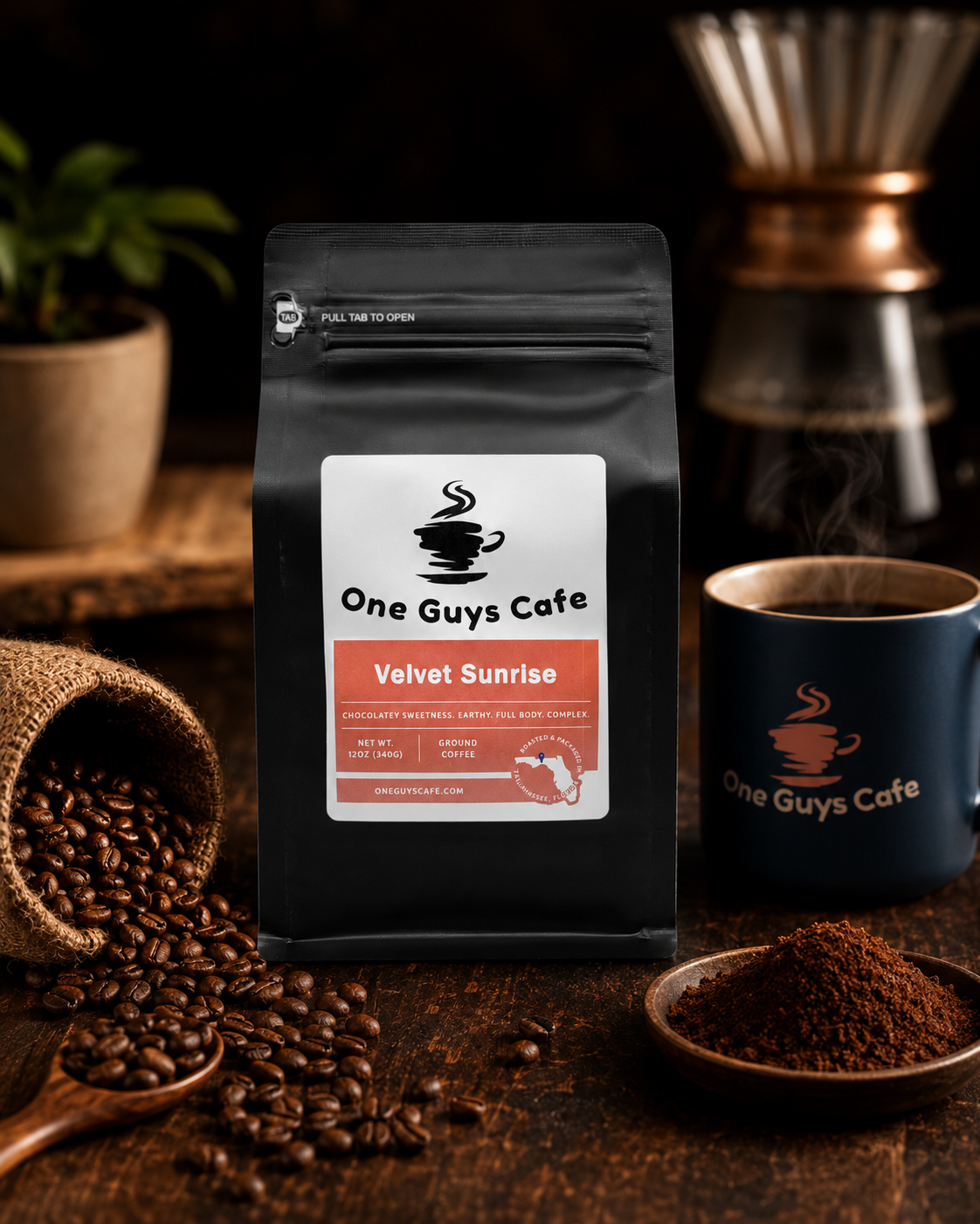 One Guys Cafe Velvet Sunrise coffee bag in a rustic coffee setting with spilled beans, ground coffee, and branded mug.